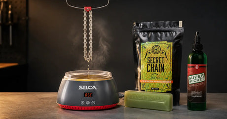 A bicycle chain hanging to drip above a wax melter with hot melt wax and drip wax alongside