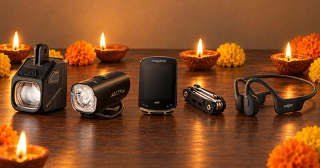 Diwali gifts for cyclists, including Magicshine bike lights, a Magene bike computer, an IceToolz multitool and Shokz headphones, laid out with lit diyas and marigolds