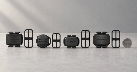 Garmin, Magene and iGPSport speed and cadence sensors laid out with their mounting bands and a coin-cell battery