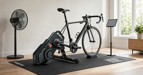 A road bike set up on a direct drive indoor trainer with a floor mat, fan and tablet